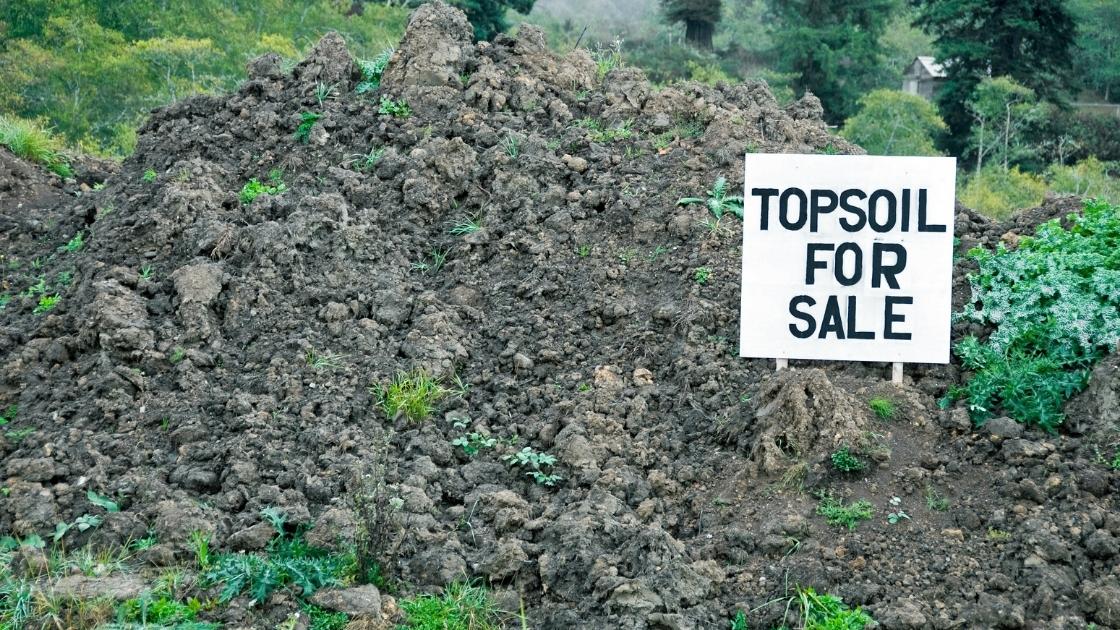 A heap of topsoil with a sign that says it is for sale