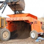 A construction vehicle busy sifting soil with an EZ-Screen topsoil screener.